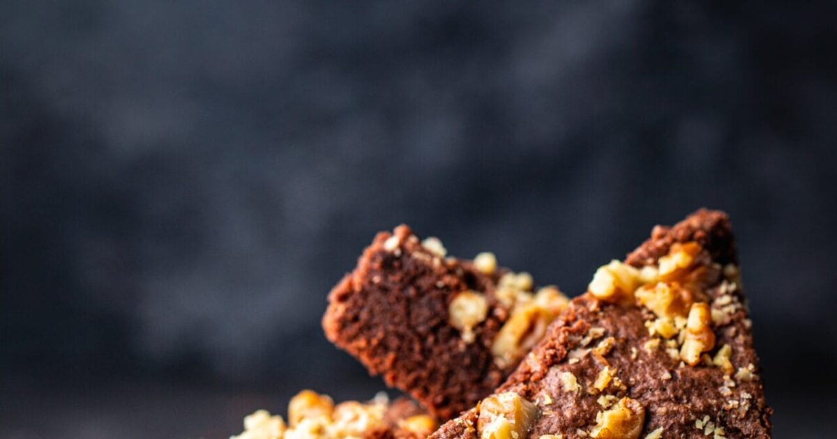 A vertical shot of a chocolate cake with walnuts in a black plate with a blurred background